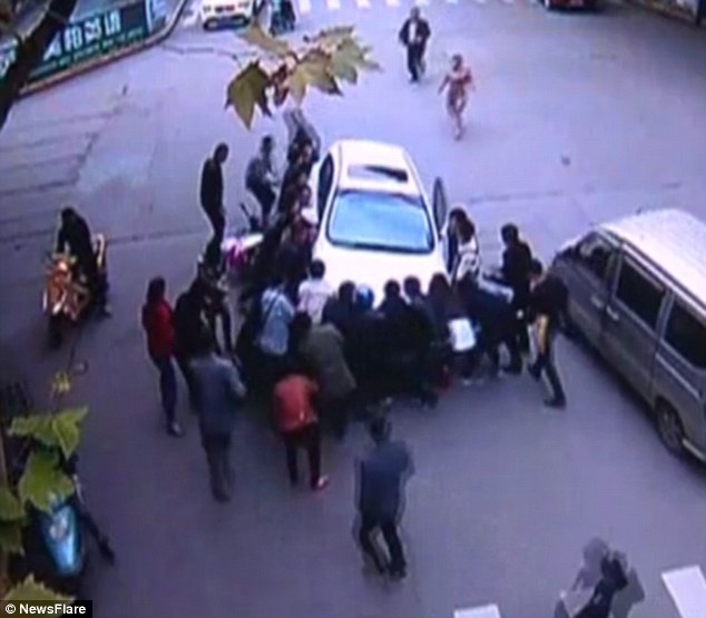 Tous à la rescousse : Plus de 20 bons samaritains se précipitent au secours de la femme pour soulever la voiture